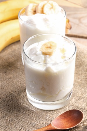 Two glasses of fat homemade yogurt with banana slices on burlap napkin.の写真素材