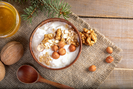 Wooden bowl with yogurt with rolled oats and nuts on burlap napkin on wooden table.の写真素材