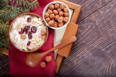 Wooden and ceramic bowls of yogurt and hazelnuts on red napkin on tray on wooden table.の写真素材