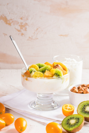 Glass bowl on stem with yogurt, sliced  fruits, whole fruits on white napkin on white backgroundの写真素材