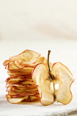 Vertical stack of apple chips and one slice standing near it on white background. Fruit chips, healthy snack, copy space.の写真素材