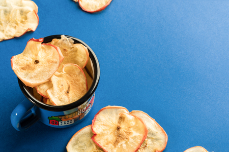 Healthy natural homemade apple chips in blue metallic mug and on bright blue background. Fruit healthy snack. Close-up, copy space.の写真素材