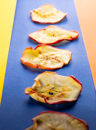 Apple chips are lying  on blue band on yellow-orange background. Perspective view, punchy pastel.の写真素材