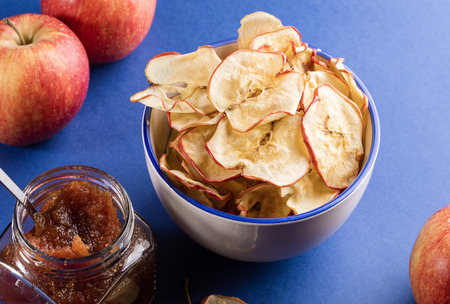 White ceramic cup with healthy homemade apple chips, fresh apples and glass jar of apple jam on...