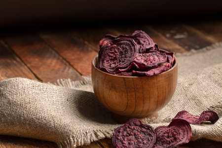 Beetroot chips in wooden bowl on burlap on wooden table on dark background.の写真素材