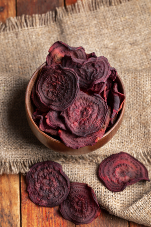 Top view beetroot chips in wooden bowl on burlap napkin on old wooden table.の写真素材