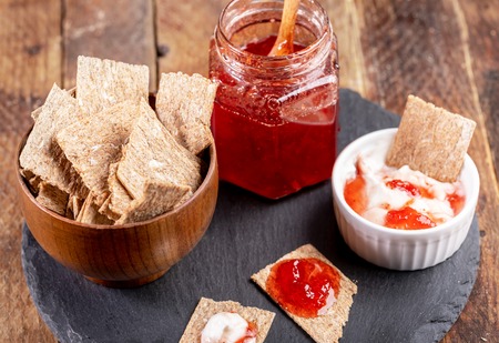 Close-up corn crispbreads with strawberry jam and sour cream on shale board on wooden background.の写真素材