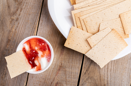 Wheat crispbreads on white plate and in bowl with sour cream and strawberry jam on wooden table.の写真素材