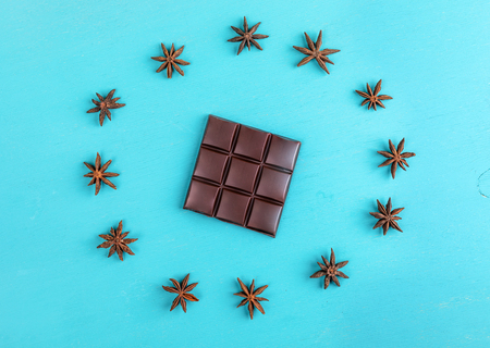 Squared bar of chocolate with stars anise laid out in circle on turquoise background.の写真素材