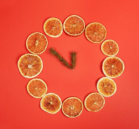 Creative Christmas handmade decor.  Dial of watch of dried orange slices with clock hands of fir twigs on red background. Minimal Xmas concept. Top view, flat lay. Square photo.の写真素材