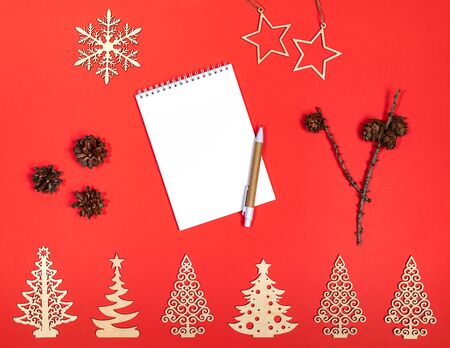 Festive Xmas mockup on red background with wooden decorations, pine cones and white notepad with pen. Flat lay, top view, copy space.の写真素材
