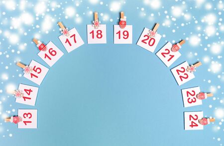 13-24 part of Advent calendar mockup with copy space. Sheets with numbers on clips laid out as arch on snowy blue.の写真素材