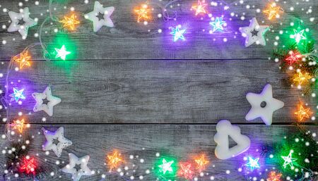 Christmas festive mockup. Xmas decorations. Creative frame of white Christmas toys stars, gingerbreads with white icing, multicolored garland with luminous stars and snow on white wooden background. Top view, flat lay, copy space.の写真素材