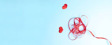 Flower from red fancifully folded ribbon and two hearts on light blue background. Valentine's day or...