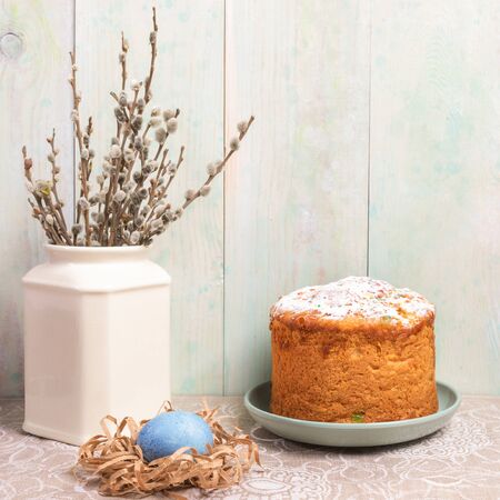 Easter composition of homemade Easter cake, blue egg in paper nest and willow branches in white vase...