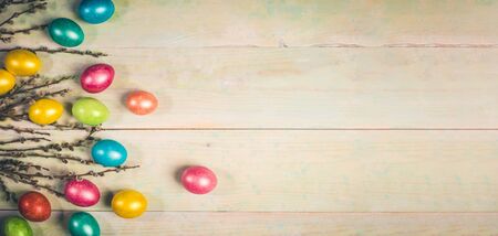 Easter festive banner with soft focus with colored Easter eggs and willow twigs on painted wooden...