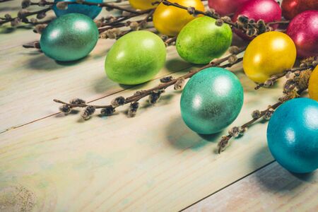 Easter festive greeting card with colored Easter eggs and willow twigs on painted wooden background...