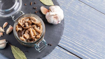 Open glass jar with homemade pickled forest honey agarics and spices on round shale board on grey wooden table. Marinated mushrooms are valuable source of protein. Fermented healthy food. Copy space.の写真素材