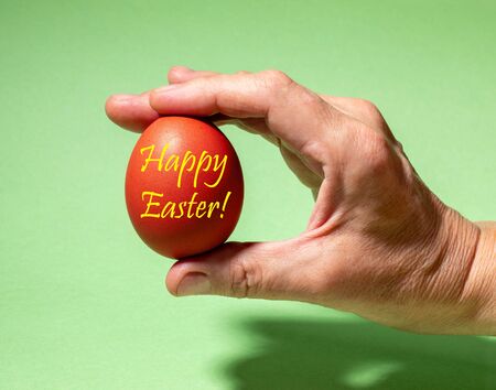 Creative easter square photo. Female hand gently holding one traditional colored red Easter egg with...