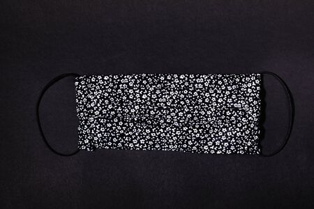 Textile handmade medical mask with black and white floral pattern on black. Mask - means of protection against virus during epidemic. Pandemic Covid-2019. Self-safety during quarantine. Top view.の写真素材