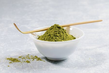 Pile with slide of green japanese matcha tea powder in white bowl with special wooden bamboo spoon...