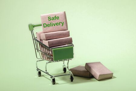 Stack of packed boxes in mini shopping trolley with label Safe Delivery and on floor. Light green Neo mint backdrop. Concept safely, contactless shopping and delivery during pandemic Covid-19.の写真素材