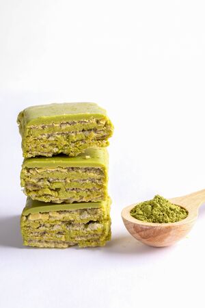 Pieces of green waffles with matcha folded in stack and wooden spoon with Matcha green tea powder on white. Matcha waffles - healthy sweet rich with antioxidants. Copy space, vertical orientation.の写真素材