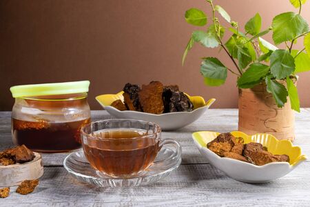 Healing infusion from birch mushroom chaga, ingredients for its cooking, birch twigs on wooden table. Chaga coffee or tea. Beverage improving immunity. Superfood. Copy space on beige backdrop.の写真素材