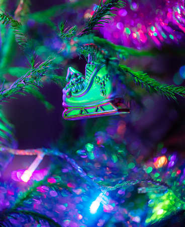 Close up xmas toy one shoe for figure skating with beautiful bokeh on Christmas tree with soft focus. Purple-blue-green trendy festive Christmas greeting card. Vertical orientation.の写真素材