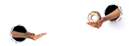 Two women hands in holes in white paper, one stretches glass Christmas toy - color donut and second...
