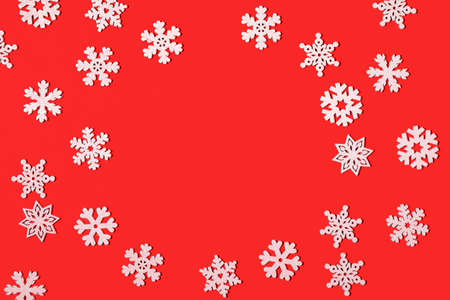 Creative Christmas flat lay composition with frame of white snowflakes on bright red backdrop....