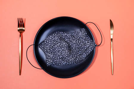 Top view one black handmade fabric protective mask with floral pattern on black plate with golden...