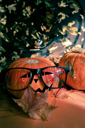 Halloween orange pumpkin painted as Jack's lantern in festive bloody glasses with fall dried maple leaf on black backdrop with ghosts. Halloween festive concept. Selective focus. Vertical orientation.の写真素材