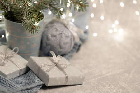 Close up cozy Christmas composition with mug fir branches, Xmas lights, DIY gift boxes, knitted Xmas ball, bokeh. Warm homely hugge atmosphere in light gray-blue color. Copy space. Selective focus.の写真素材
