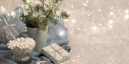 Xmas composition with fir twigs in mug, Xmas lights, DIY gift box, marshmallow, snowflakes on knitted gray plaid. Cozy warm homely winter Danish hygge concept. Selective focus. Copy space.の写真素材