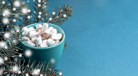 Cup of coffee or cocoa with marshmallows and fir branches with drawn snow on turquoise close up. Home cozy holiday concept. Christmas background. Horizontal orientation. Copy space for text.の写真素材