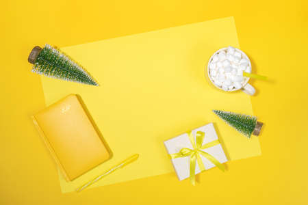Christmas workspace backdrop. Yellow notepad - organizer on 2021, small Xmas trees, cup of coffee...