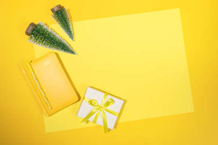 Yellow Christmas workspace backdrop. Frame of yellow notepad - organizer on 2021, small Xmas trees...