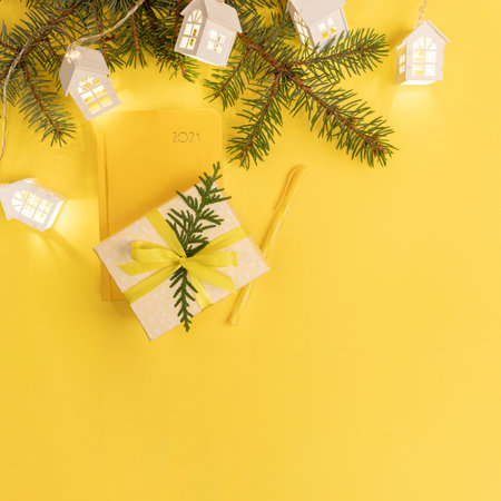 Xmas business greeting card. Yellow notepad on 2021, fir branches, shining Xmas lights white lodges, gift box on yellow. Planning for next year. Top view. Copy space for text. Square image.の写真素材