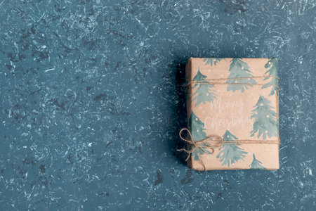 One gift box wrapped in festive Xmas wrapping paper on turquoise textured background. Safe delivery...