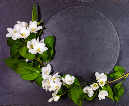 Empty shale round black serving board with white apple tree twig. Festive mockup for serving or recipes on spring holidays. Valentine's Day, Mother's Day, Birthday. Top view, copy space.の写真素材