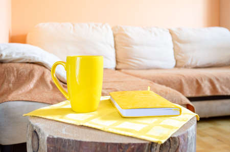 Trendy minimal home cozy interior with light corner sofa, creative wooden stump as table with yellow cup and notepad.の写真素材