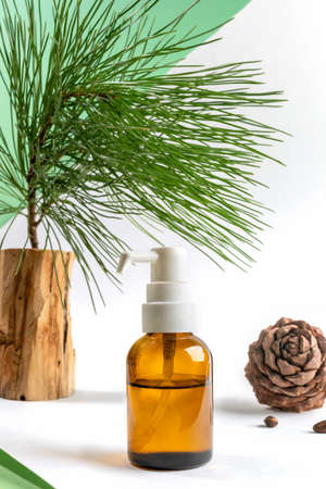 Small glass bottle with dispenser of essential cedar oil, cedar branch and cone on white-green background. Herbal medicine and spa coniferous products concept. Vertical orientation.の写真素材