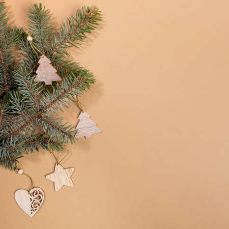 Christmas or New Year festive layout with green fir tree branches and festive wooden craft decorations - Xmas toys on beige backdrop with copy space. Top view. Square photo.の写真素材