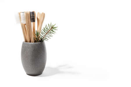 Wooden toothbrushes in gray cup, natural soap, fir twig, textile pouch, white snowflakes on wooden stumps on white background. Selective focus. Xmas self-care, sustainable lifestyle. Copy space.の写真素材
