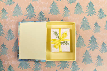 Open box with Christmas DIY wrapped gift box inside it on festive backdrop. Copy space. Top view....