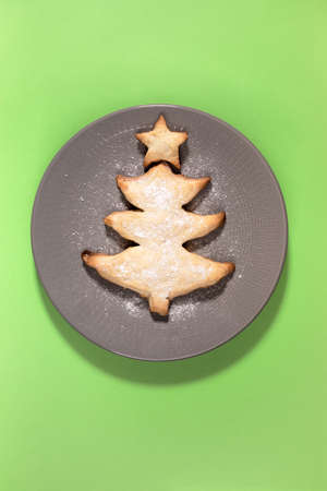 Homemade creative baked cookie as Christmas tree on round gray plate on green background. Holiday...