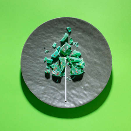 Creative sweet Christmas tree made of pieces of fractured green lollipop on textured gray plate on...