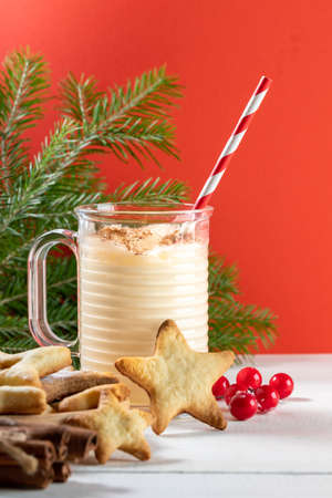 Christmas image with traditional hot drink eggnog in glass mug, ginger cookies, green fir branches,...