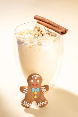 Traditional hot Christmas drink - homemade creamy eggnog with cinnamon in glass with double walls with gingerbread man on beige neutral background. Xmas beverage image. Close up. Vertical orientation.の写真素材